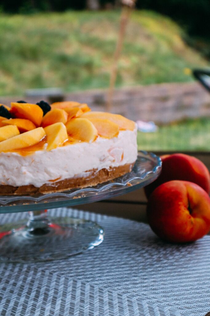 Cheesecale alle pesche su alzata di vetro, usata come foto in vetrina.