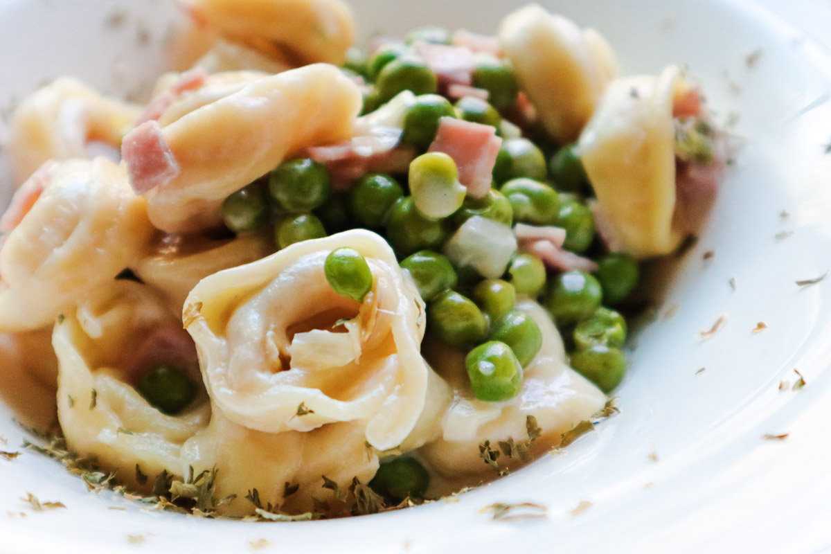 Primo piano del piatto con tortellini, prosciutto e piselli freschi e verdi.