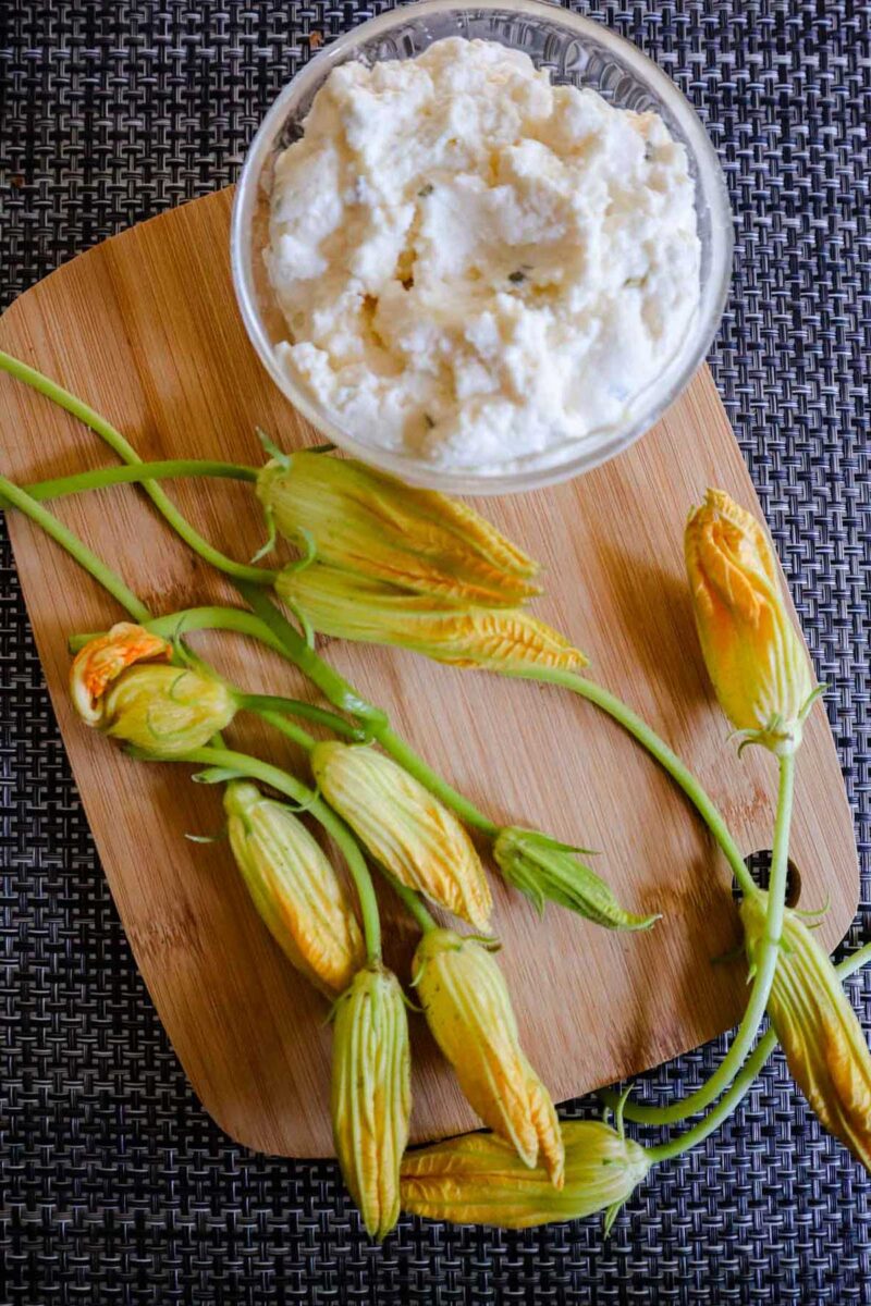 Foto dei fiori di zucca puliti con ingredienti su tagliere di legno.